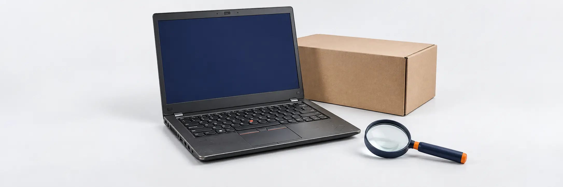 Een openstaande laptop met een vergrootglas en een kartonnen doos op een witte achtergrond.